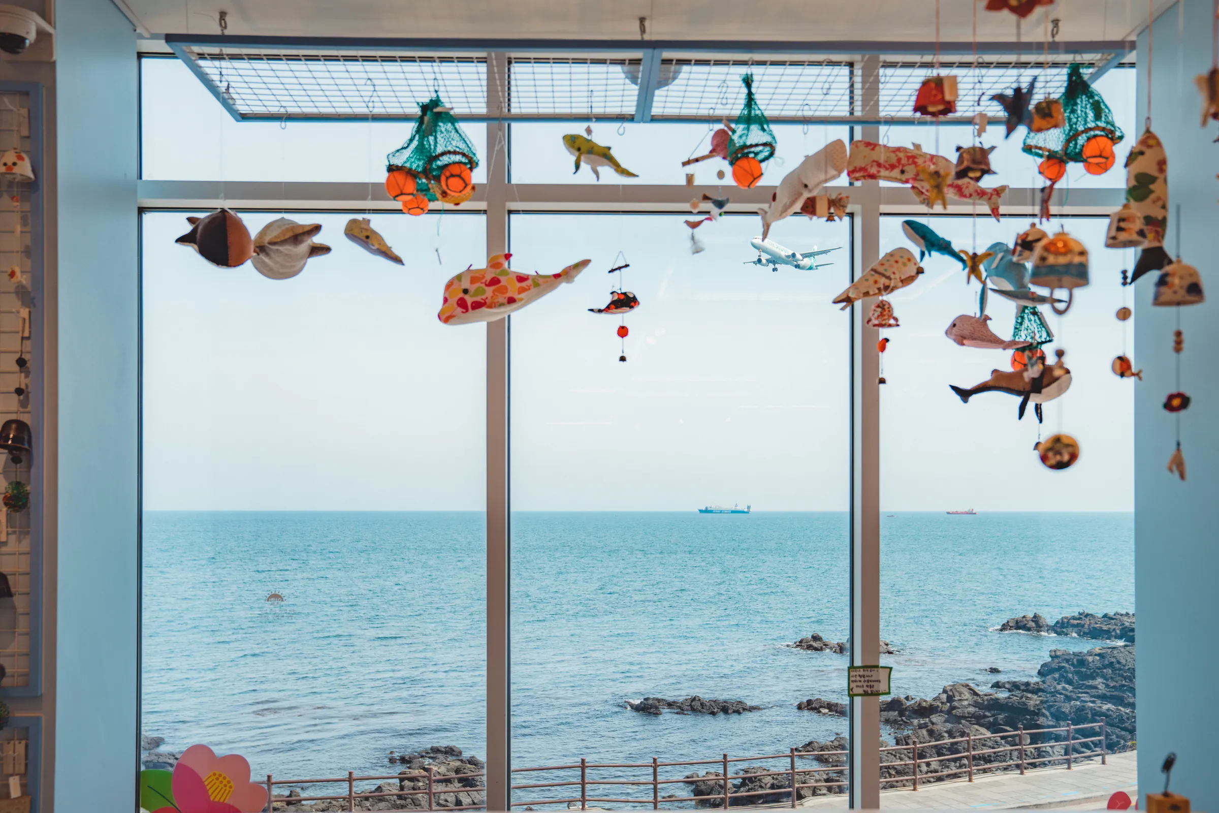 창 너머 제주 바다와 천장에 매달린 해녀복 모빌